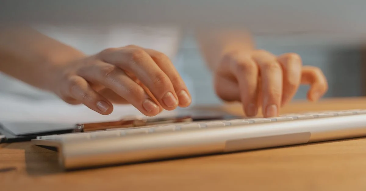 Gros plan sur des mains tapant sur un clavier blanc, mettant en avant la technologie moderne et la productivité.