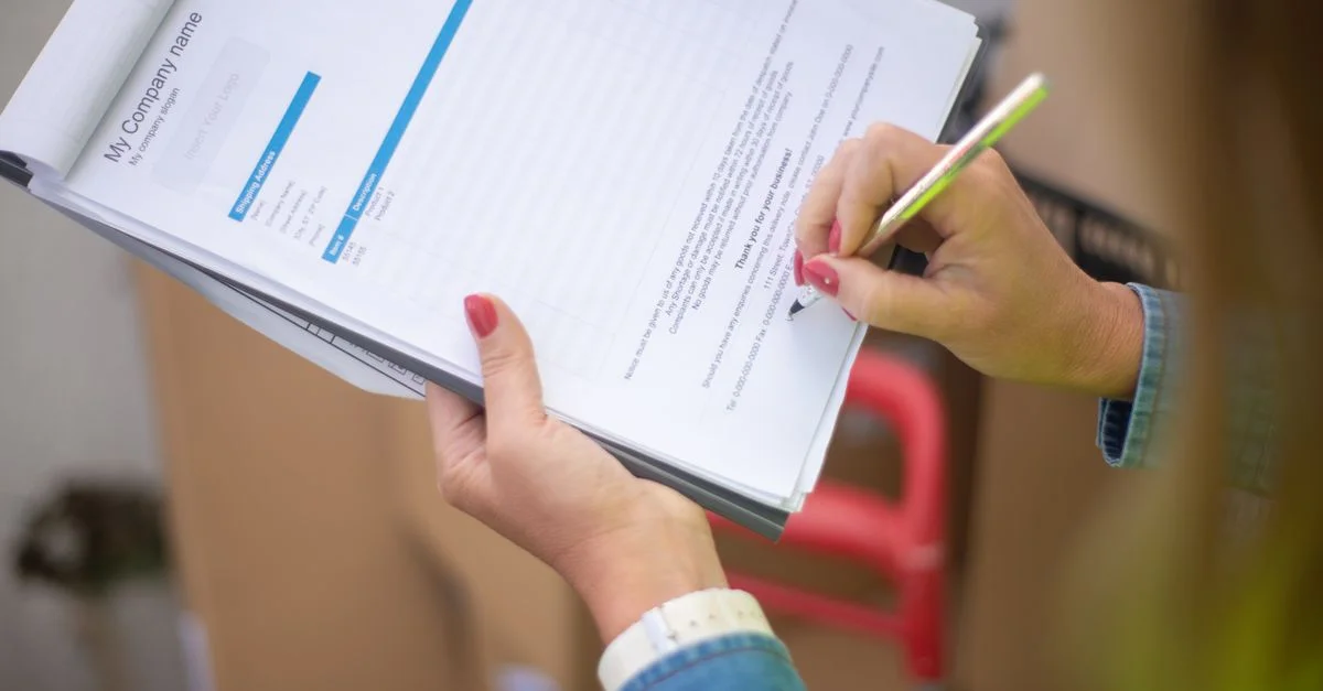 Gros plan sur la main d'une femme signant un document sur un classeur. Idéal pour des thèmes commerciaux et juridiques.